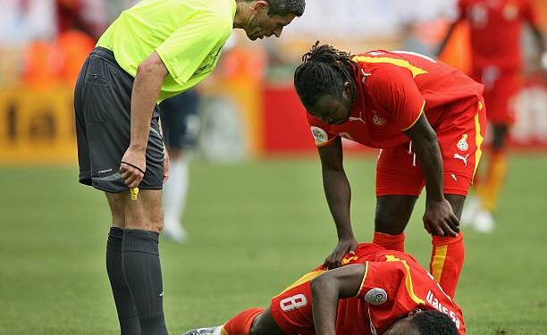 NUREMBERG, GERMANY - JUNE 22:  Michael Essien of Ghana lies injured under the gaze of referee Markus Merk and Razak Pimpong of Ghana during the FIFA World Cup Germany 2006 match between Ghana and USA played at the Stadium Nuernberg on June 22, 2006 in Nuremberg, Germany.  (Photo by Clive Brunskill/Getty Images)